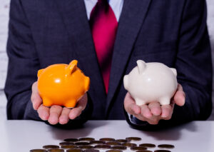 An image of a business man holding two different piggy banks, comparing the two.