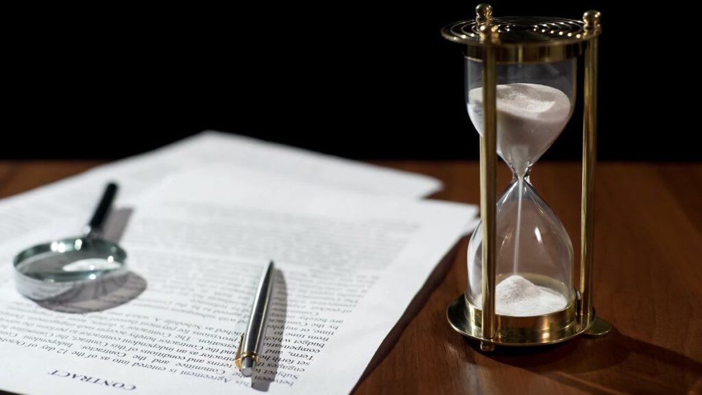 Photo of an hourglass and a contract on a desk.